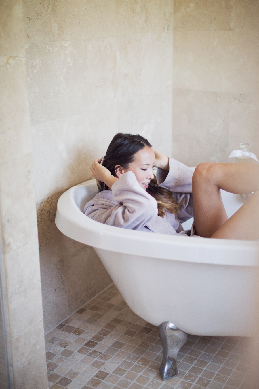 Girl in bathrobe in bathtub in bathroom playing with hair